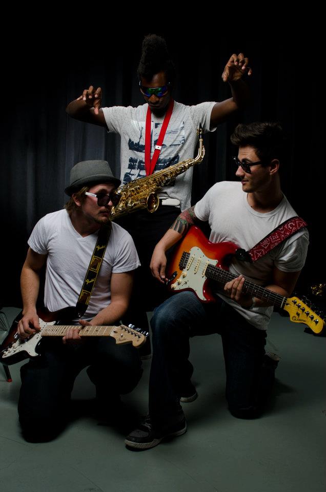 Three band members posing with guitars and saxophone